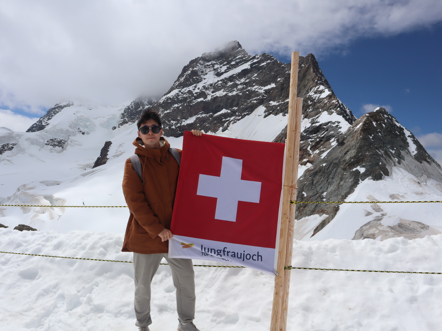 Xinlong Du standing by the Jungfraujoch sign with snowy mountains behind him